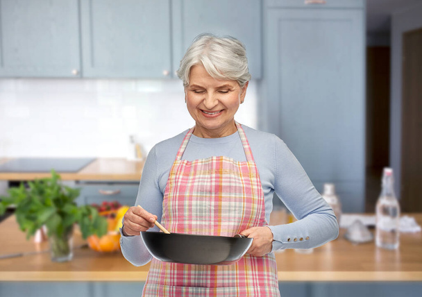 smiling senior woman in apron with frying pan - Fotografie, Obrázek