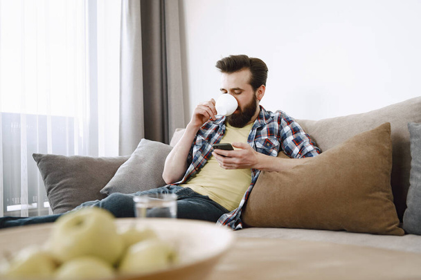 Man drinking coffee and watching TV on couch - Fotoğraf, Görsel
