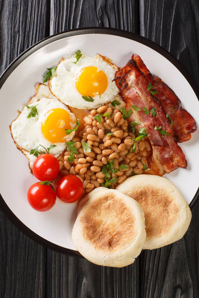 Englantilainen aamiainen paistettuja munia, papuja, pekonia, tomaatteja ja muffineja lähikuva lautasella pöydällä. pystysuora ylhäältä näkymä abov - Valokuva, kuva