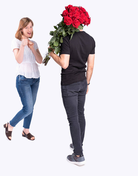 The handsome girl is glad to see her boyfriend carrying a beautiful bouquet of her favorite flowers. - Foto, Imagen