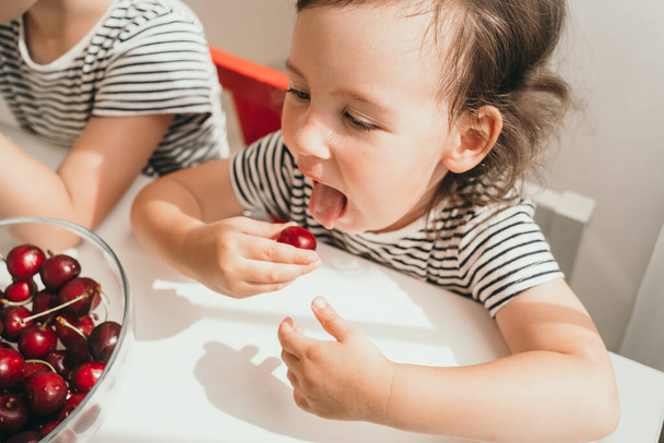 A gyerek finom, lédús bogyókat eszik. Közelkép egy kislányról, aki eszik. Egy csíkos pólós gyerek gyümölcsöt eszik. Vicces gyerek megmutatja a nyelvét.. - Fotó, kép