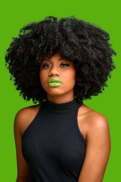 black girl with afro hair style looking at camera, photographed over green background. - Foto, Imagem