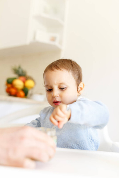 Funny little baby boy in the kitchen eating fruit puree from a bottle all dirty face.kitchen lifestyle, close up. - Foto, immagini