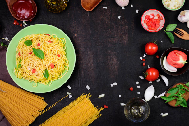 Klasszikus olasz spagetti tészta egy ínycsiklandozó zöld ételben. Paradicsom szósszal és bazsalikomos fokhagymás hagymával spagetti paradicsom fa kanál és villa elhelyezni egy sötét fekete fa asztal. - Fotó, kép