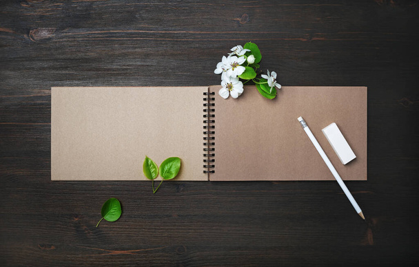 Photo of blank kraft sketchbook, pencil, eraser and spring flowers on wooden background. Template for placing your design. Flat lay. - Fotografie, Obrázek