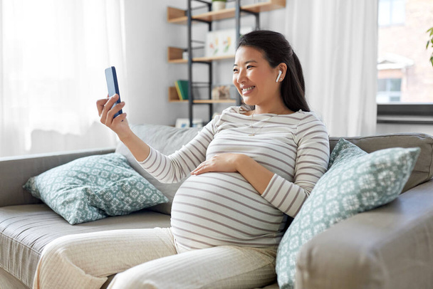 pregnant woman with phone and earphones at home - Foto, immagini