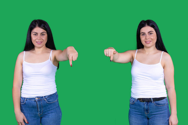 Two amazing beautiful girls are standing on distance and showing down with their index finger over a green background. - Foto, imagen