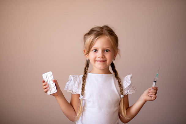 little girl with pigtails smiles and holds pills and syringe in her hands, plays a children's doctor. Health concept, Treatment and vaccination of children, taking medicine, hospital, pediatrics - Foto, imagen