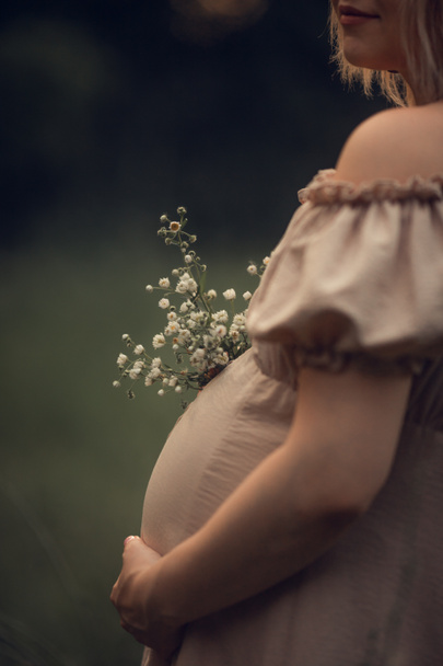 uma mulher grávida com um vestido bege segura uma mão em uma barriga. À espera de um bebé, sessão de fotos grávidas. gravidez e parto no verão, 9 meses. conceito de maternidade - Foto, Imagem