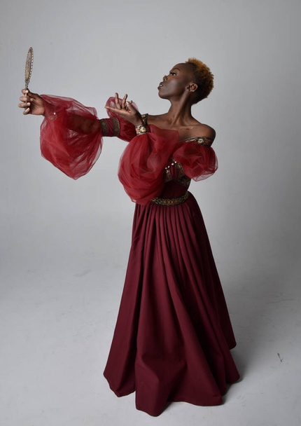 Ritratto a figura intera di bella donna africana che indossa lungo abito di fantasia medievale rinascimentale rosso, in piedi posa su uno sfondo grigio chiaro studio. - Foto, immagini