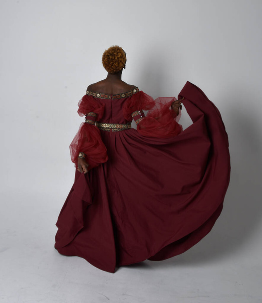 Plně dlouhý portrét krásné africké ženy v dlouhých červených renesančních středověkých fantasy šatech, stojící póza na světle šedém pozadí studia. - Fotografie, Obrázek