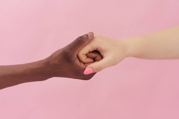 Caucasian woman and African-American man holding hands together on pink background. Racism concept - Photo, Image