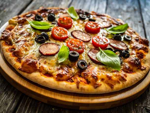 Pizza with white mushrooms, sausage, tomatoes, black olives, parmesan and mozzarella on wooden background  - Foto, imagen
