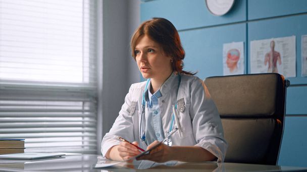 Médica jovem escreve prescrição e conversa com paciente explicando diagnóstico contra parede do hospital - Foto, Imagem