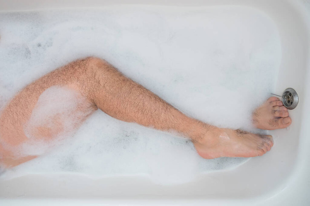 Lustiges Bild eines Mannes, der ein entspannendes Bad nimmt. Nahaufnahme männlicher Füße in einem Schaumbad. Ansicht von oben - Foto, Bild