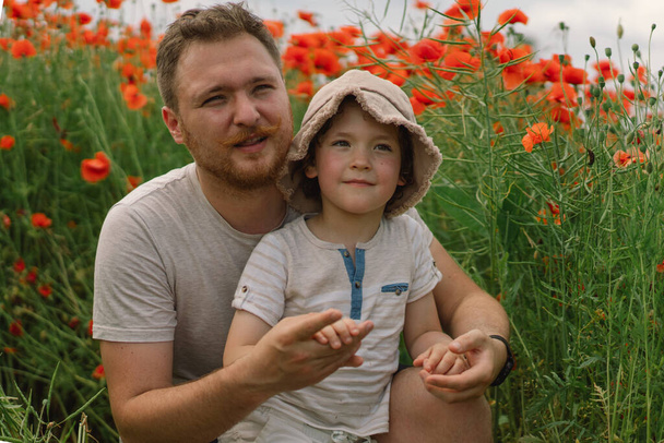 Happy fathers day. Little boy and father are playing in a beautiful field of red poppies. - Photo, Image