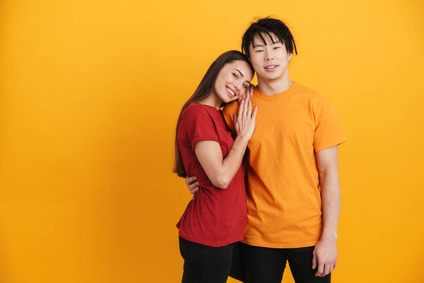 Young multiracial couple smiling and hugging while posing on camera isolated over yellow wall - Valokuva, kuva