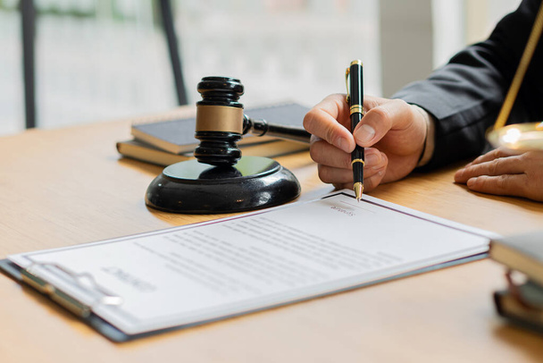 Un abogado que trabaja en una oficina y una báscula de martillo y oro de un juez delante con un cuaderno en una mesa de concepto de asesor legal. - Foto, Imagen