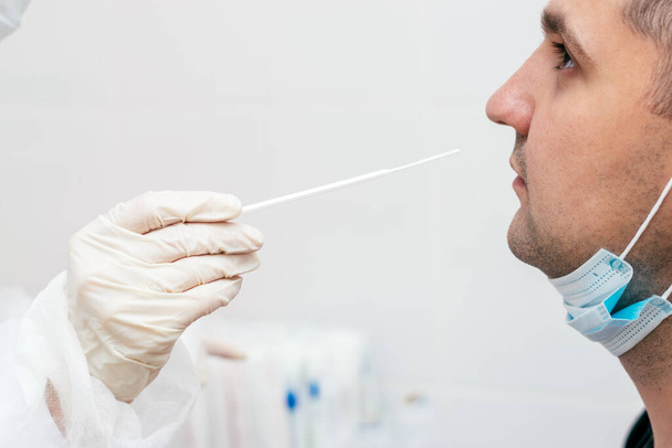 Un trabajador médico que toma un hisopo nasal del hombre de mediana edad para detectar una posible infección por coronavirus en la clínica.Concepto médico y coronavirus. - Foto, imagen