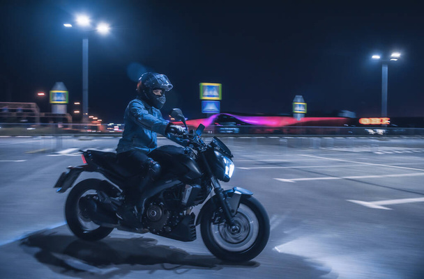 Motorcyclist sits on a motorbike in neon light in an empty parking lot at night - Фото, изображение