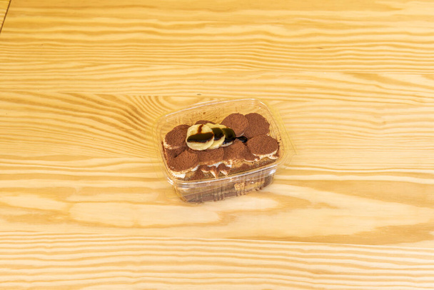 İtalyan tiramisu tatlısının üzerinde muz dilimleri kakao tozu ve çikolata şurubuyla kaplı. - Fotoğraf, Görsel