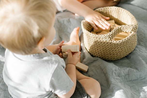 Baby boy sitting on bed playing with wooden toy. Kids hands holding a wooden rectangular blocks. Eco friendly, zero waste concept. - Foto, immagini