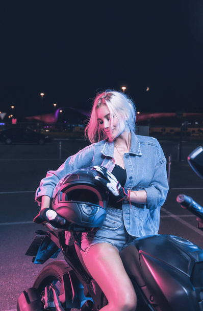 portrait of a girl in the rays of neon light on a motorbike at night in an empty parking lot - Fotografie, Obrázek