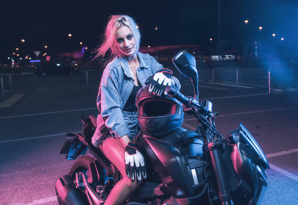 portrait of a girl in the rays of neon light on a motorbike at night in an empty parking lot - Fotoğraf, Görsel