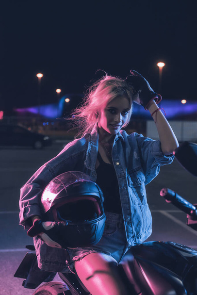 portrait of a girl in the rays of neon light on a motorbike at night in an empty parking lot - 写真・画像