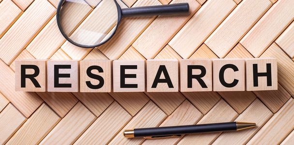 Wooden cubes with the word RESEARCH stand on a wooden background between a magnifying glass and a pen - Fotó, kép