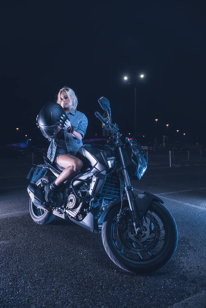 portrait of a girl in the rays of neon light on a motorbike at night in an empty parking lot - Photo, image
