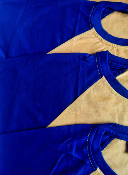 Beige shirt with dark blue sleeves. a pile or arrangement of brownish-yellow T-shirts with navy blue sleeves and collars - Photo, Image