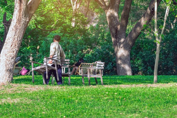 Back view of Asian male waiter prepare chairs for customers to sit and relax in the garden. Summer vacation in green surroundings. Happy outdoors relaxing on chair in garden. Outdoor leisure. - Photo, Image