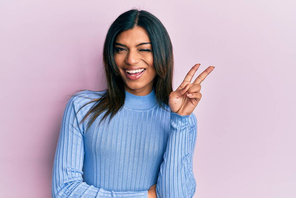 Young latin transsexual transgender woman wearing casual clothes smiling with happy face winking at the camera doing victory sign. number two.  - Photo, Image