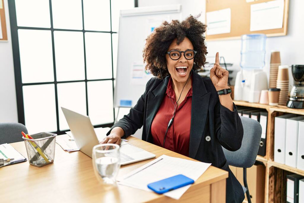 Mujer afroamericana con cabello afro trabajando en la oficina con auriculares de operador apuntando con el dedo hacia arriba con una idea exitosa. exitado y feliz. número uno.  - Foto, Imagen