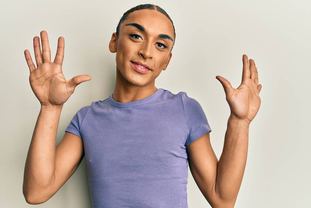 Hispanic man wearing make up and long hair wearing casual t shirt showing and pointing up with fingers number ten while smiling confident and happy.  - Photo, Image