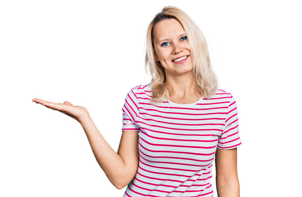Young caucasian woman wearing casual clothes smiling cheerful presenting and pointing with palm of hand looking at the camera.  - Photo, Image