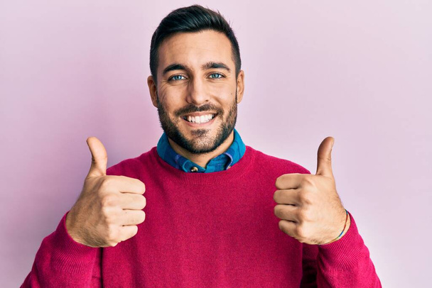Young hispanic man wearing casual clothes success sign doing positive gesture with hand, thumbs up smiling and happy. cheerful expression and winner gesture.  - Photo, Image