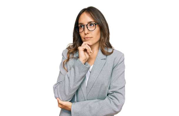 Young brunette woman wearing business clothes with hand on chin thinking about question, pensive expression. smiling with thoughtful face. doubt concept.  - Fotoğraf, Görsel