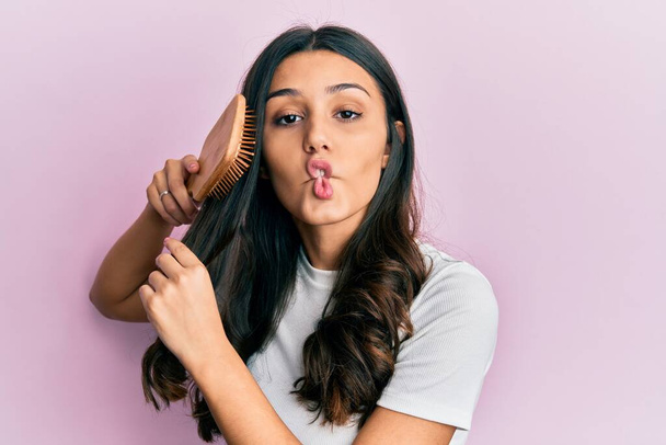 Nuori latino nainen muotoilu hiukset käyttäen kampa tehdä kalan kasvot suulla ja siristää silmät, hullu ja koominen.  - Valokuva, kuva