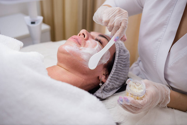 Nahaufnahme eines Kosmetikers, der eine Gesichtsmaske für einen Kunden herstellt - Foto, Bild