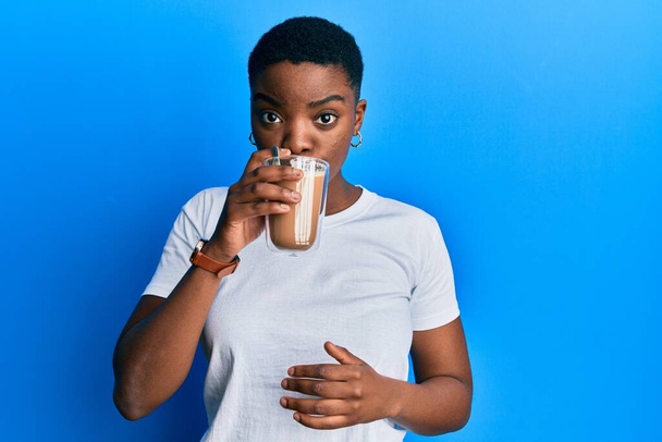 Mujer afroamericana joven bebiendo taza de café sobre fondo azul aislado - Foto, imagen