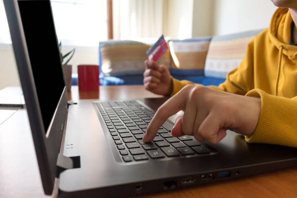 Personne méconnaissable achats en ligne, sur leur ordinateur portable avec une carte de crédit rouge, dans un salon. - Photo, image