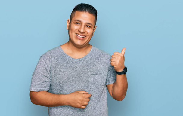Young latin man wearing casual clothes smiling with happy face looking and pointing to the side with thumb up.  - Foto, Imagen