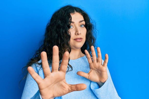 Young brunette woman with curly hair wearing casual clothes afraid and terrified with fear expression stop gesture with hands, shouting in shock. panic concept.  - Foto, afbeelding