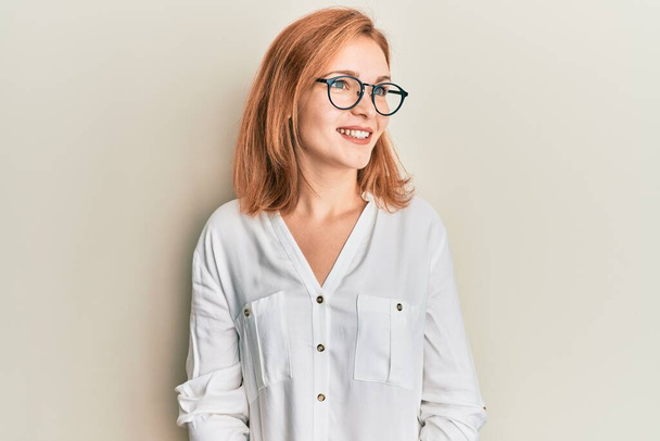 Junge kaukasische Frau in lässiger Kleidung und Brille, die zur Seite schaut, entspannte Profil-Pose mit natürlichem Gesicht und selbstbewusstem Lächeln.  - Foto, Bild
