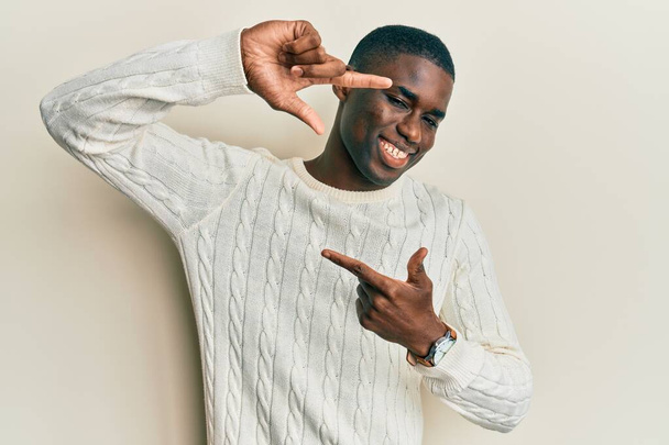 Young african american man wearing casual clothes smiling making frame with hands and fingers with happy face. creativity and photography concept.  - Fotó, kép