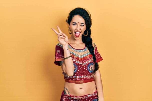 Young woman wearing bindi and bollywood clothing smiling with happy face winking at the camera doing victory sign. number two.  - Φωτογραφία, εικόνα