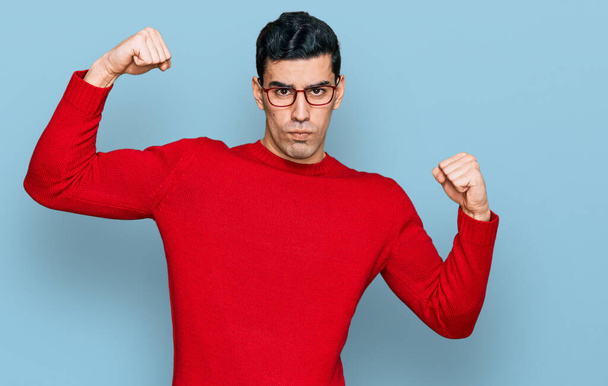 Hombre hispano guapo usando ropa casual y gafas que muestran los músculos de los brazos sonriendo orgulloso. concepto de fitness.  - Foto, Imagen