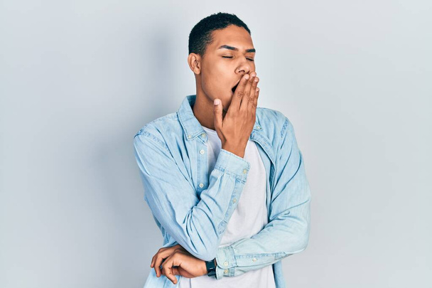 Młody Afroamerykanin w luźnych ciuchach znudzony ziewaniem, zakrywający usta dłonią. niepokój i senność.  - Zdjęcie, obraz